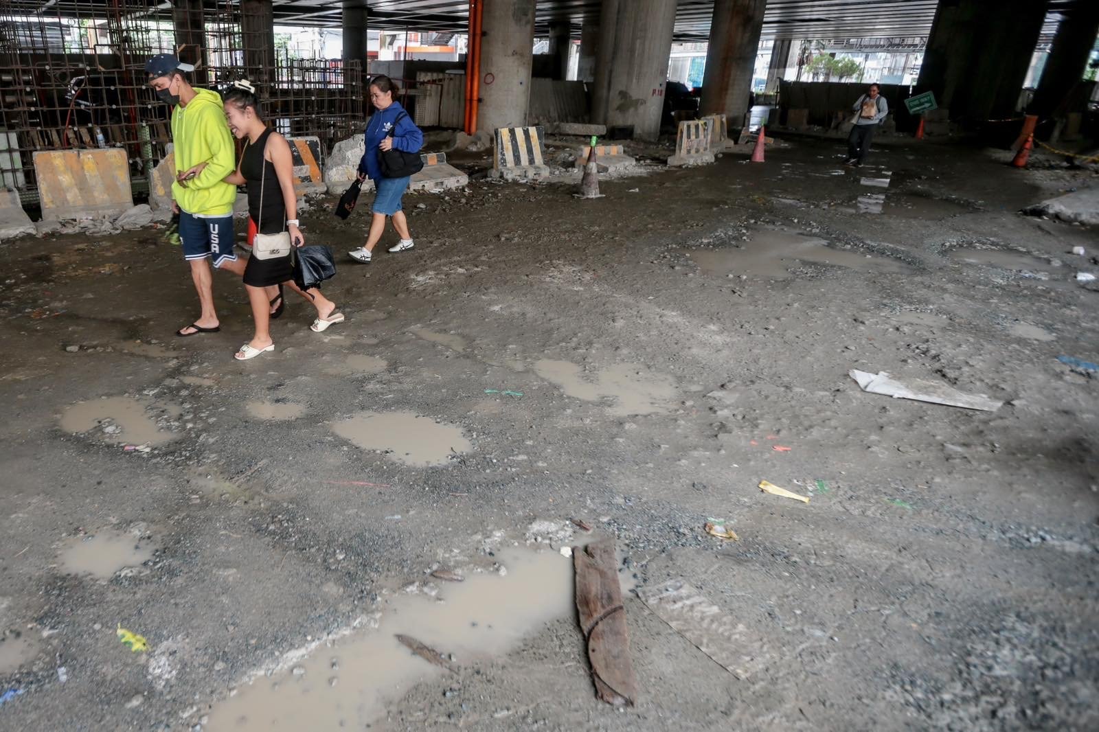 Pedestrians struggle to navigate a muddy, soil-covered road beneath a construction site leading to the MRT North Avenue station in Quezon City. | Aram Lascano