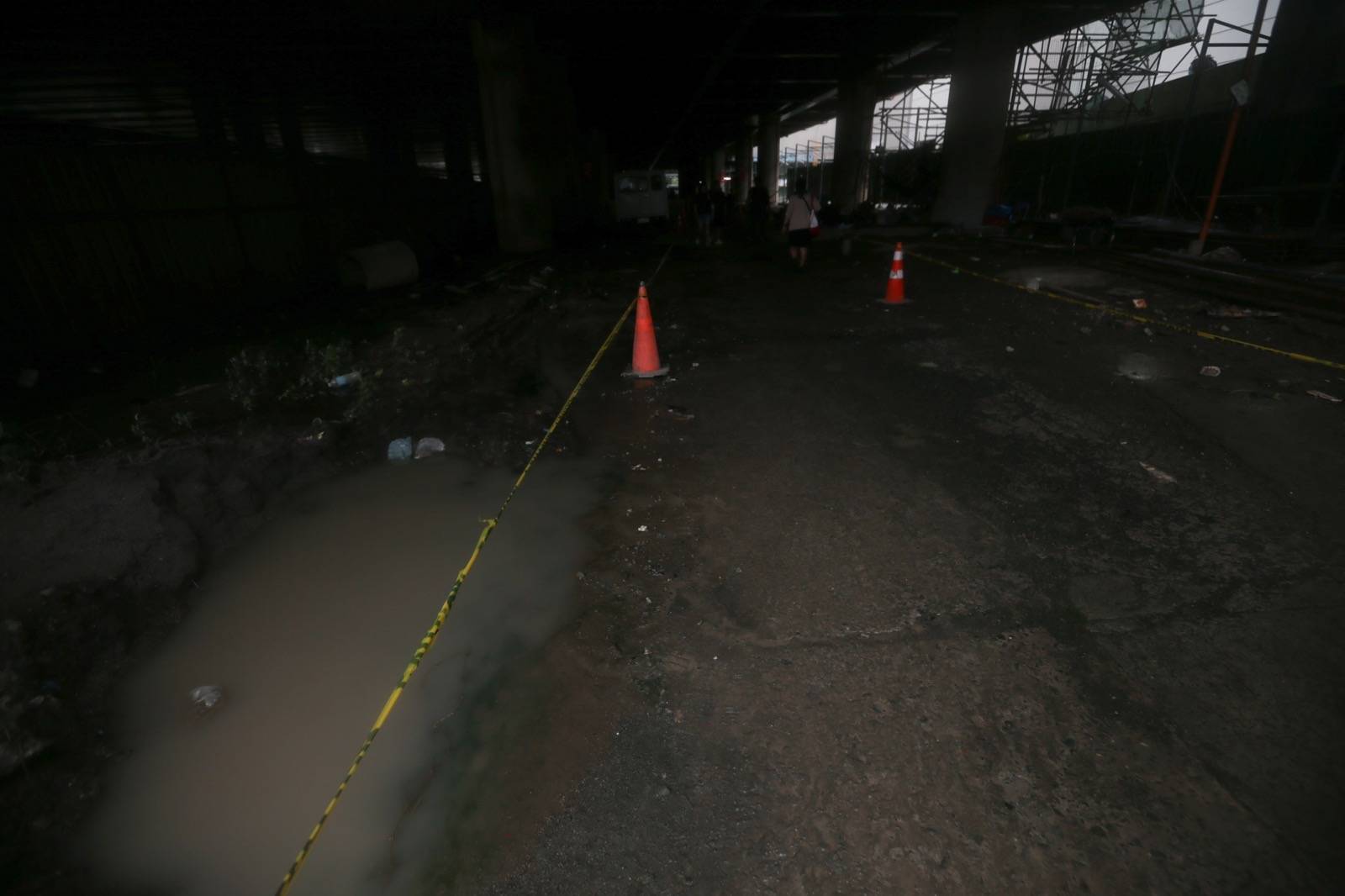Pedestrians struggle to navigate a muddy, soil-covered road beneath a construction site leading to the MRT North Avenue station in Quezon City. | Aram Lascano