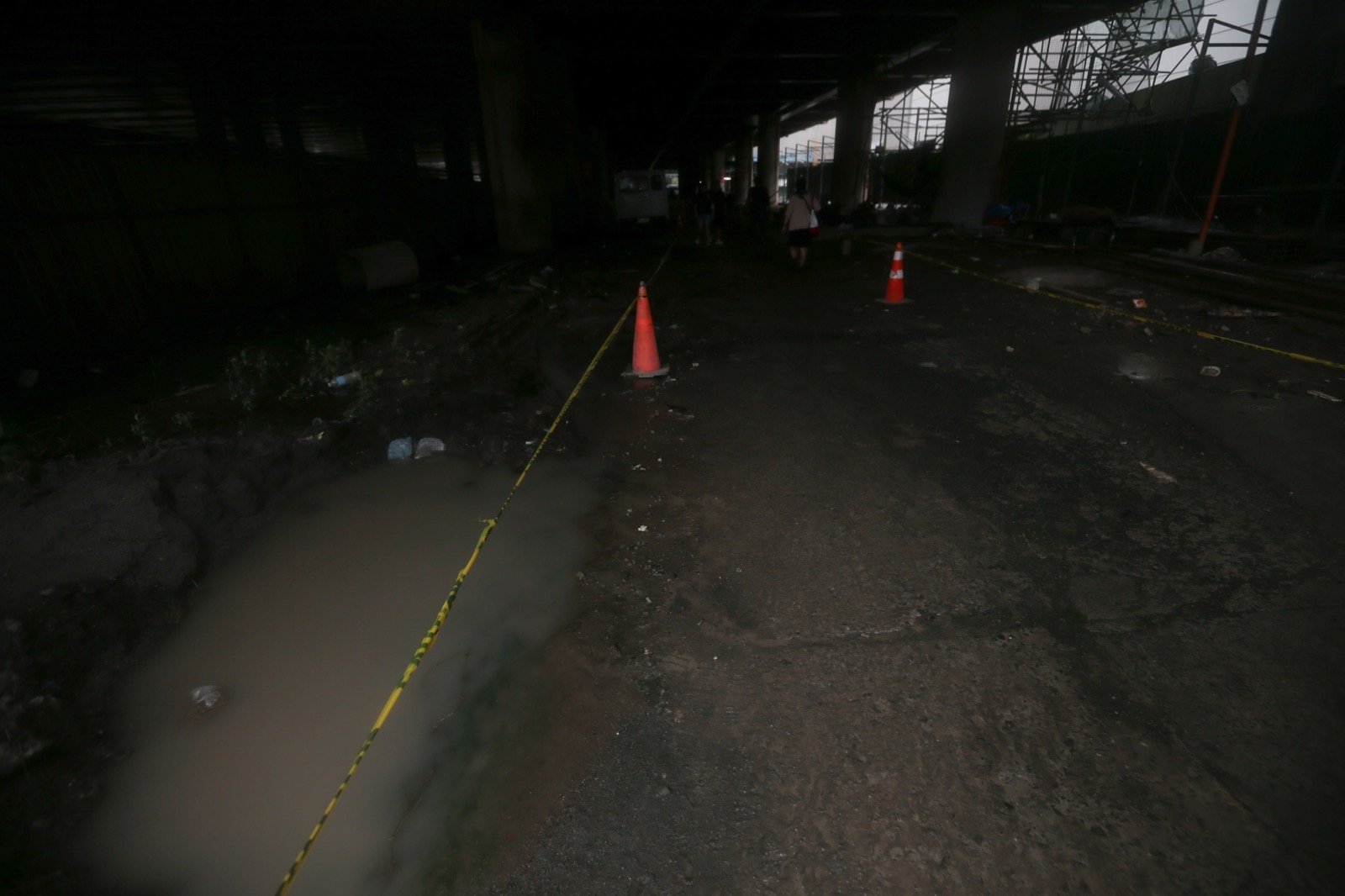 Pedestrians struggle to navigate a muddy, soil-covered road beneath a construction site leading to the MRT North Avenue station in Quezon City. | Aram Lascano