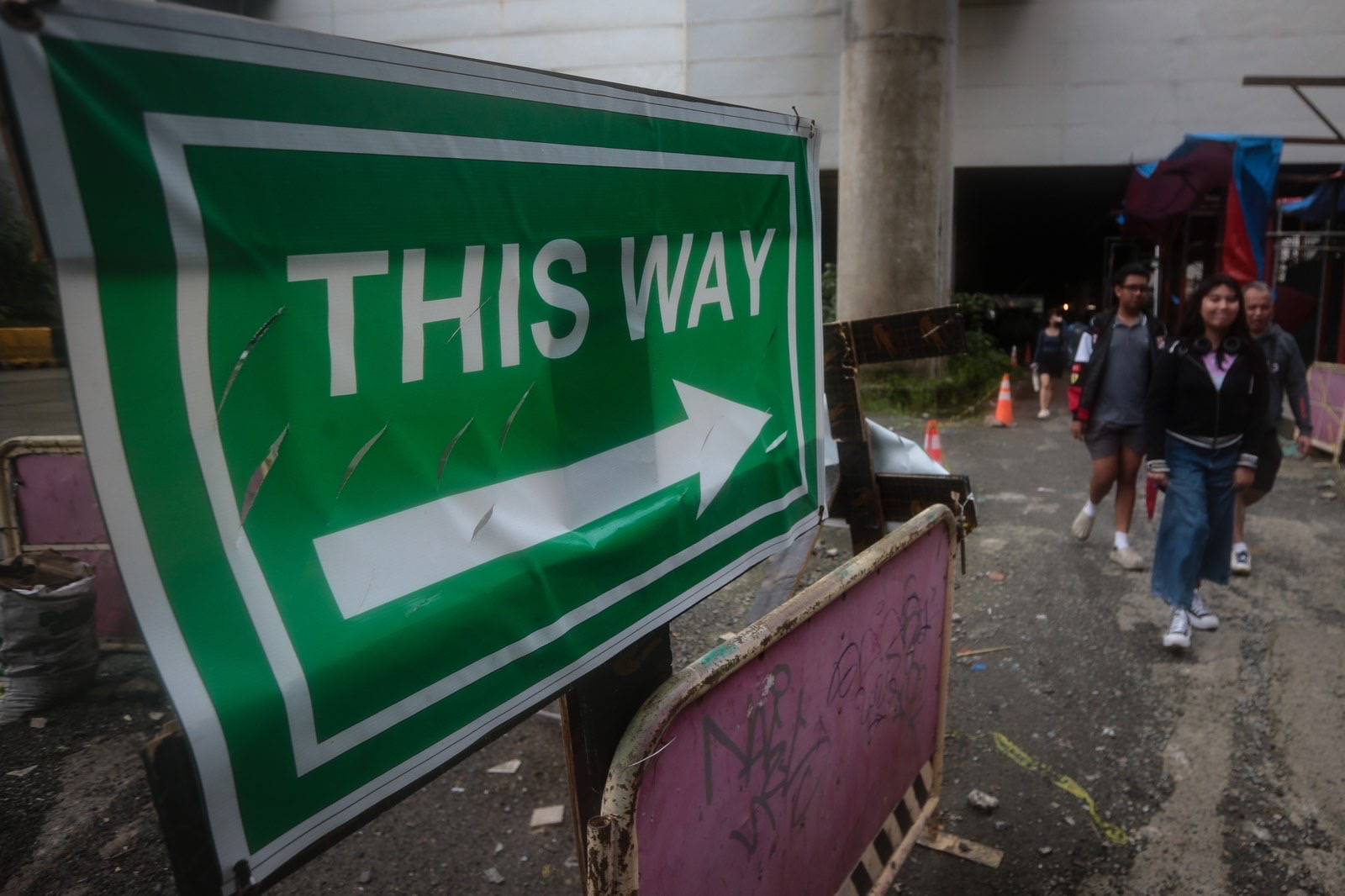 Pedestrians struggle to navigate a muddy, soil-covered road beneath a construction site leading to the MRT North Avenue station in Quezon City. | Aram Lascano