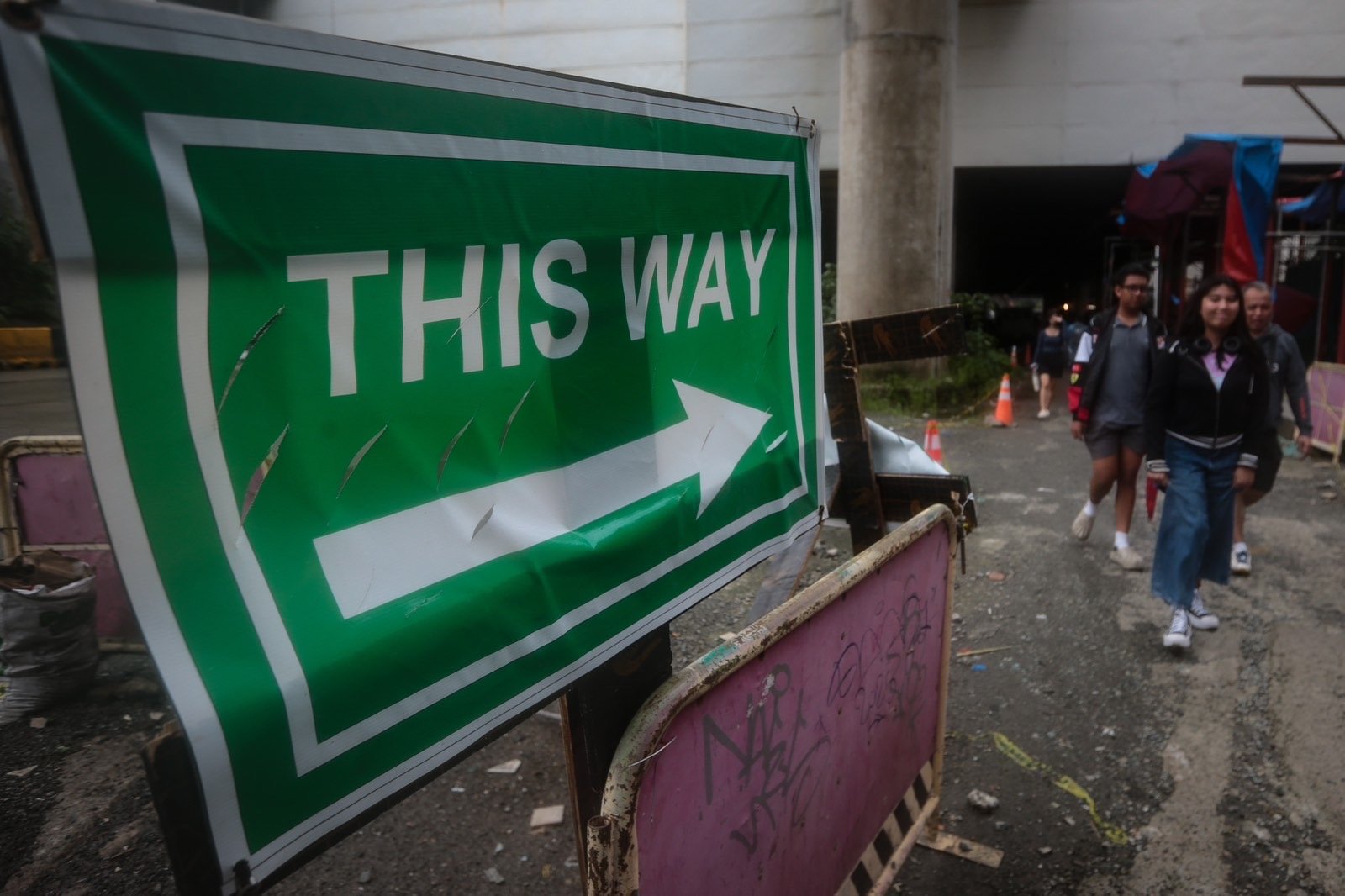 Pedestrians struggle to navigate a muddy, soil-covered road beneath a construction site leading to the MRT North Avenue station in Quezon City. | Aram Lascano