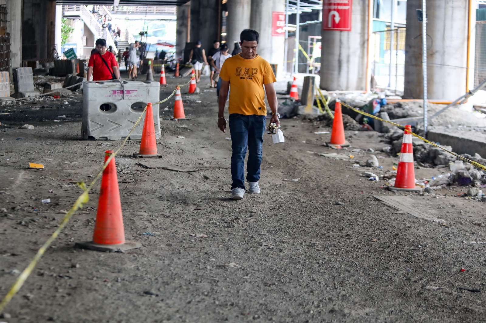 Pedestrians struggle to navigate a muddy, soil-covered road beneath a construction site leading to the MRT North Avenue station in Quezon City. | Aram Lascano