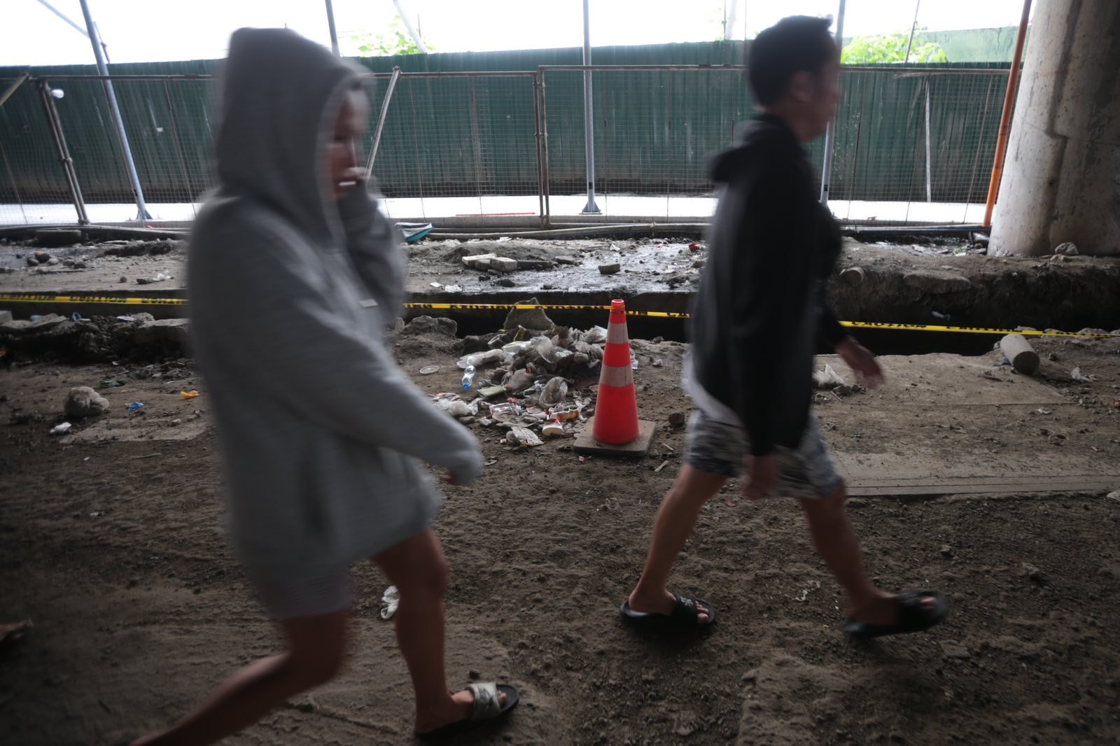 Pedestrians struggle to navigate a muddy, soil-covered road beneath a construction site leading to the MRT North Avenue station in Quezon City. | Aram Lascano