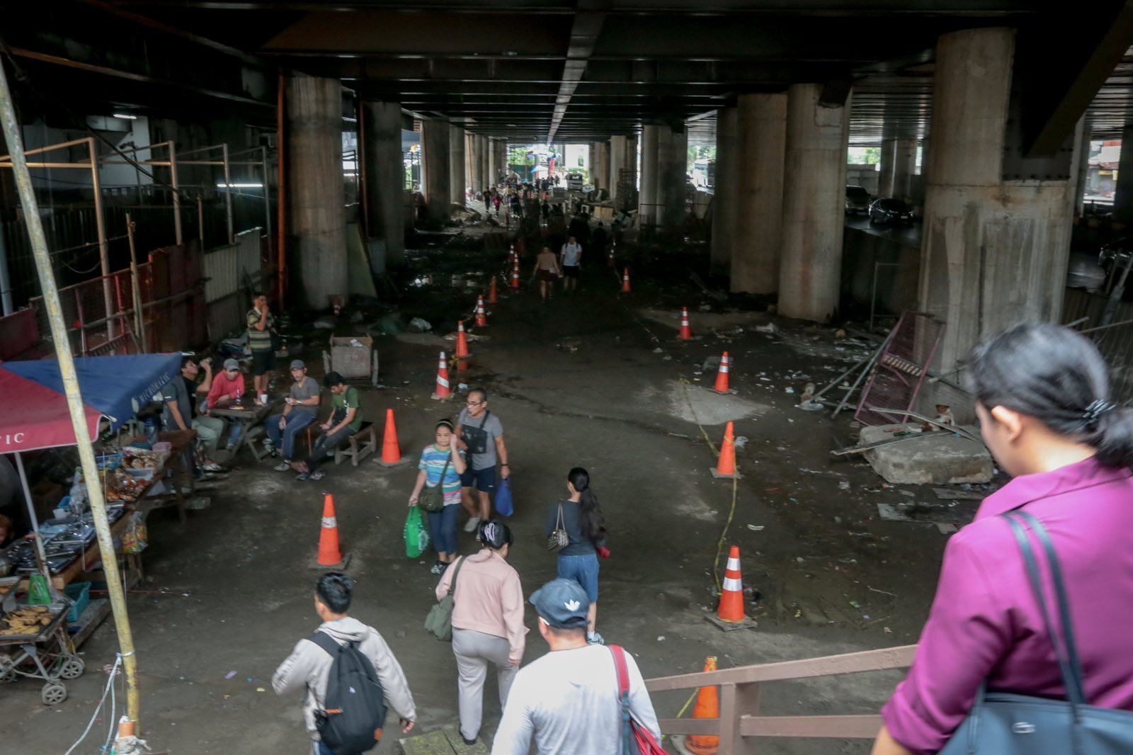 Pedestrians struggle to navigate a muddy, soil-covered road beneath a construction site leading to the MRT North Avenue station in Quezon City. | Aram Lascano