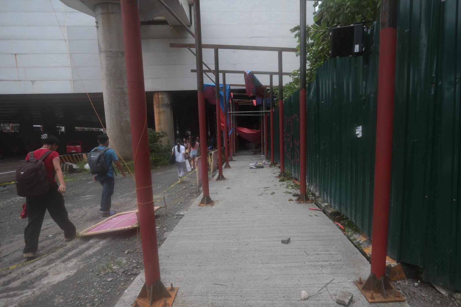 Pedestrians struggle to navigate a muddy, soil-covered road beneath a construction site leading to the MRT North Avenue station in Quezon City. | Aram Lascano