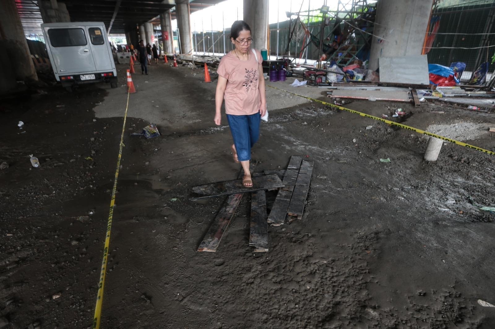 Pedestrians struggle to navigate a muddy, soil-covered road beneath a construction site leading to the MRT North Avenue station in Quezon City. | Aram Lascano