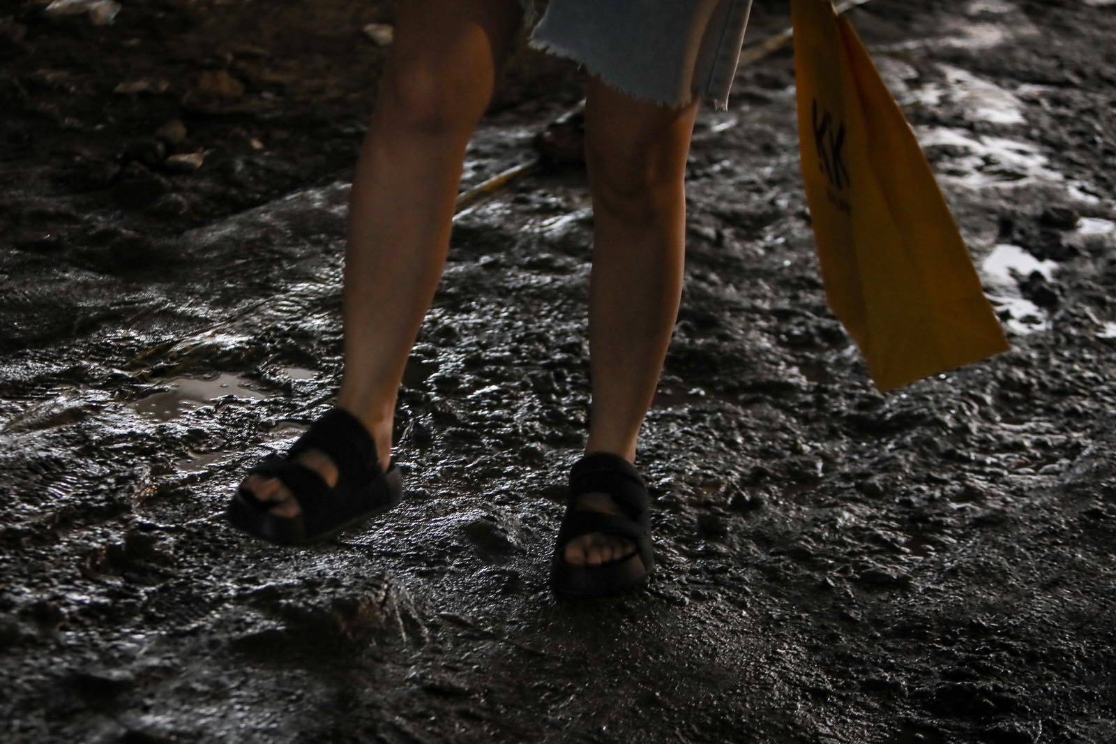 Pedestrians struggle to navigate a muddy, soil-covered road beneath a construction site leading to the MRT North Avenue station in Quezon City. | Aram Lascano