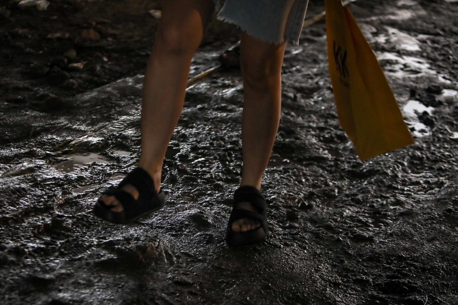 Pedestrians struggle to navigate a muddy, soil-covered road beneath a construction site leading to the MRT North Avenue station in Quezon City. | Aram Lascano