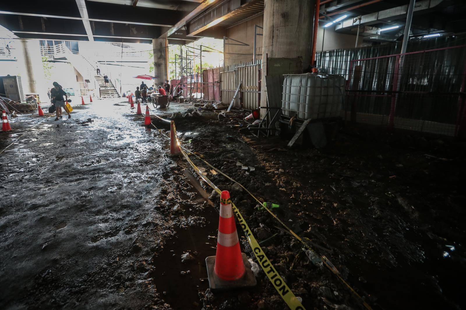 Pedestrians struggle to navigate a muddy, soil-covered road beneath a construction site leading to the MRT North Avenue station in Quezon City. | Aram Lascano