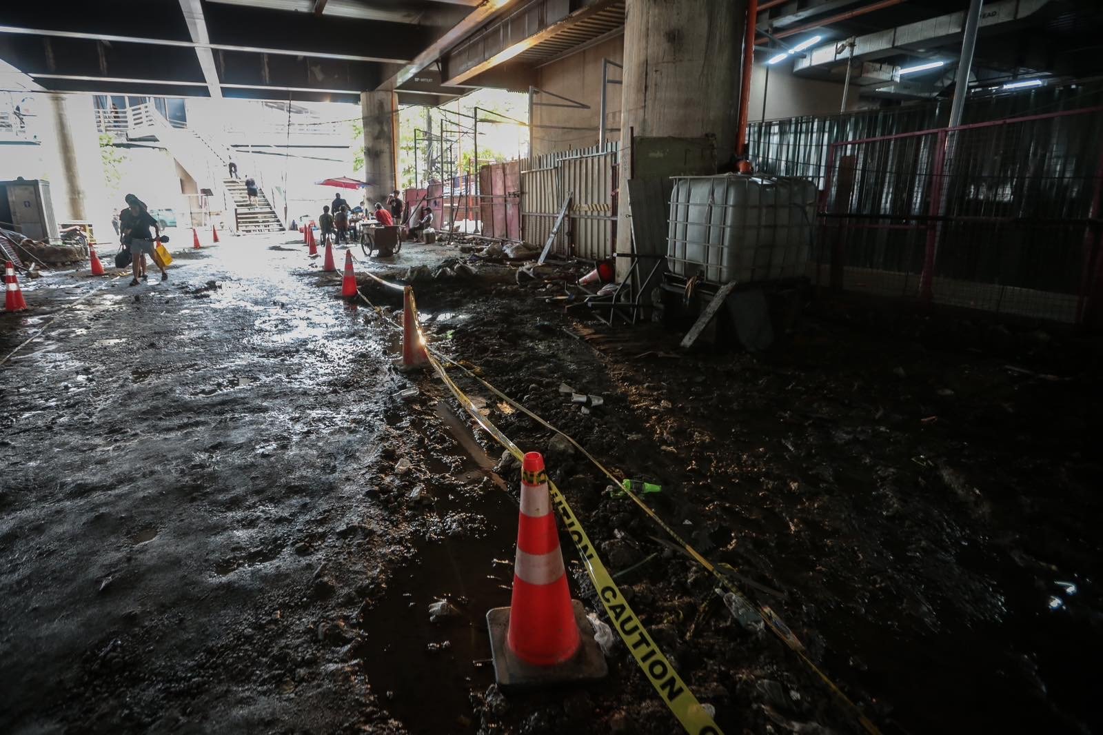 Pedestrians struggle to navigate a muddy, soil-covered road beneath a construction site leading to the MRT North Avenue station in Quezon City. | Aram Lascano
