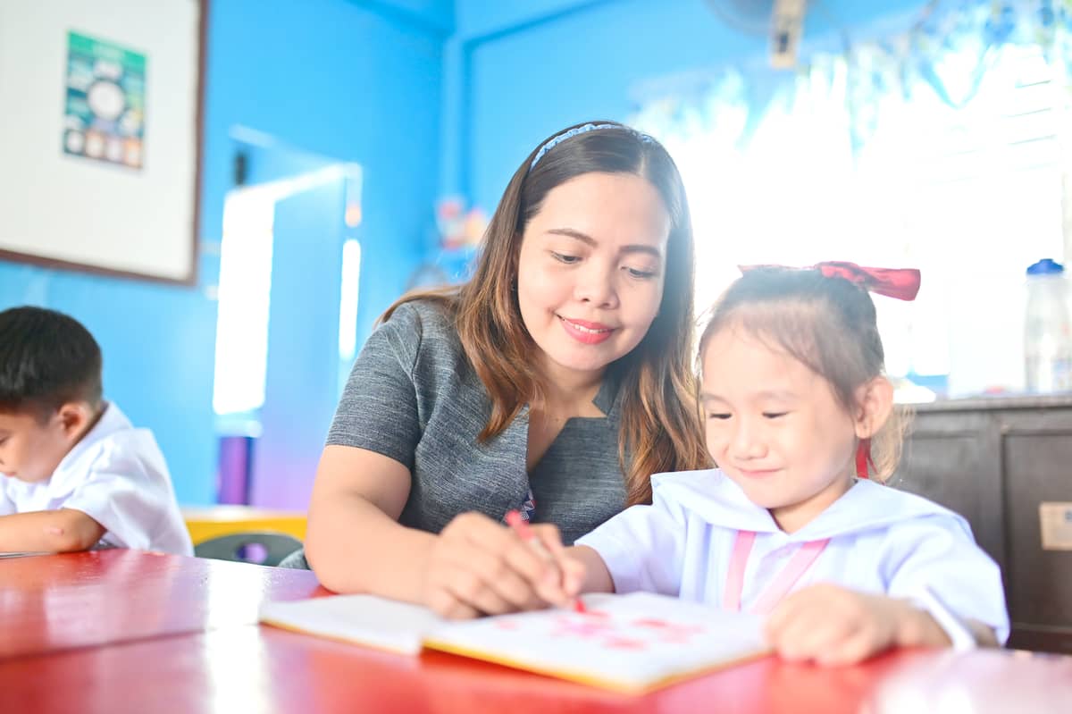 Teacher III Rizalyn Rico guides a student during a class activity inside the newly rehabilitated building at Jugan Elementary School. The safer, more resilient learning space, supported by SM Foundation, gives teachers and learners greater confidence as they return to their daily routines following the 2025 earthquake.