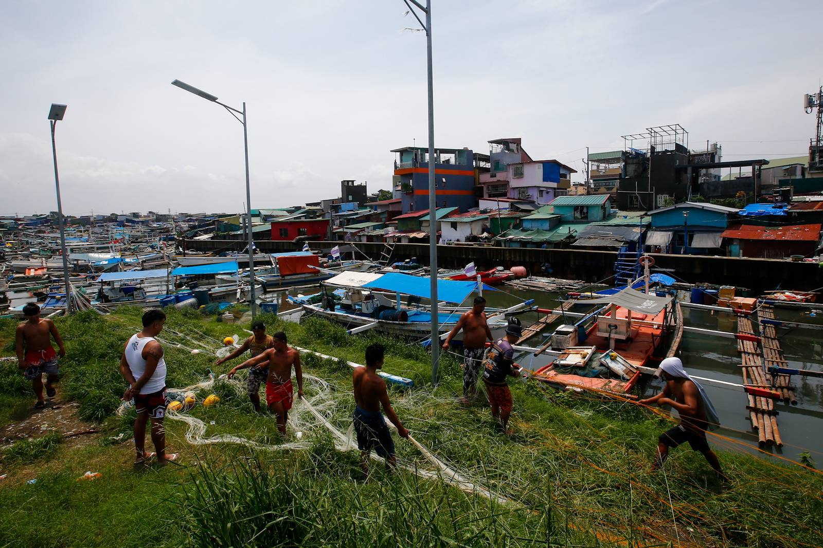 As the sun finally emerges, a group of fishermen make fishing nets at a vacant lot in Navotas City on 15 August 2026. Strong waves and heavy rains brought by the southwest monsoon, or habagat, have kept them from sailing for weeks.