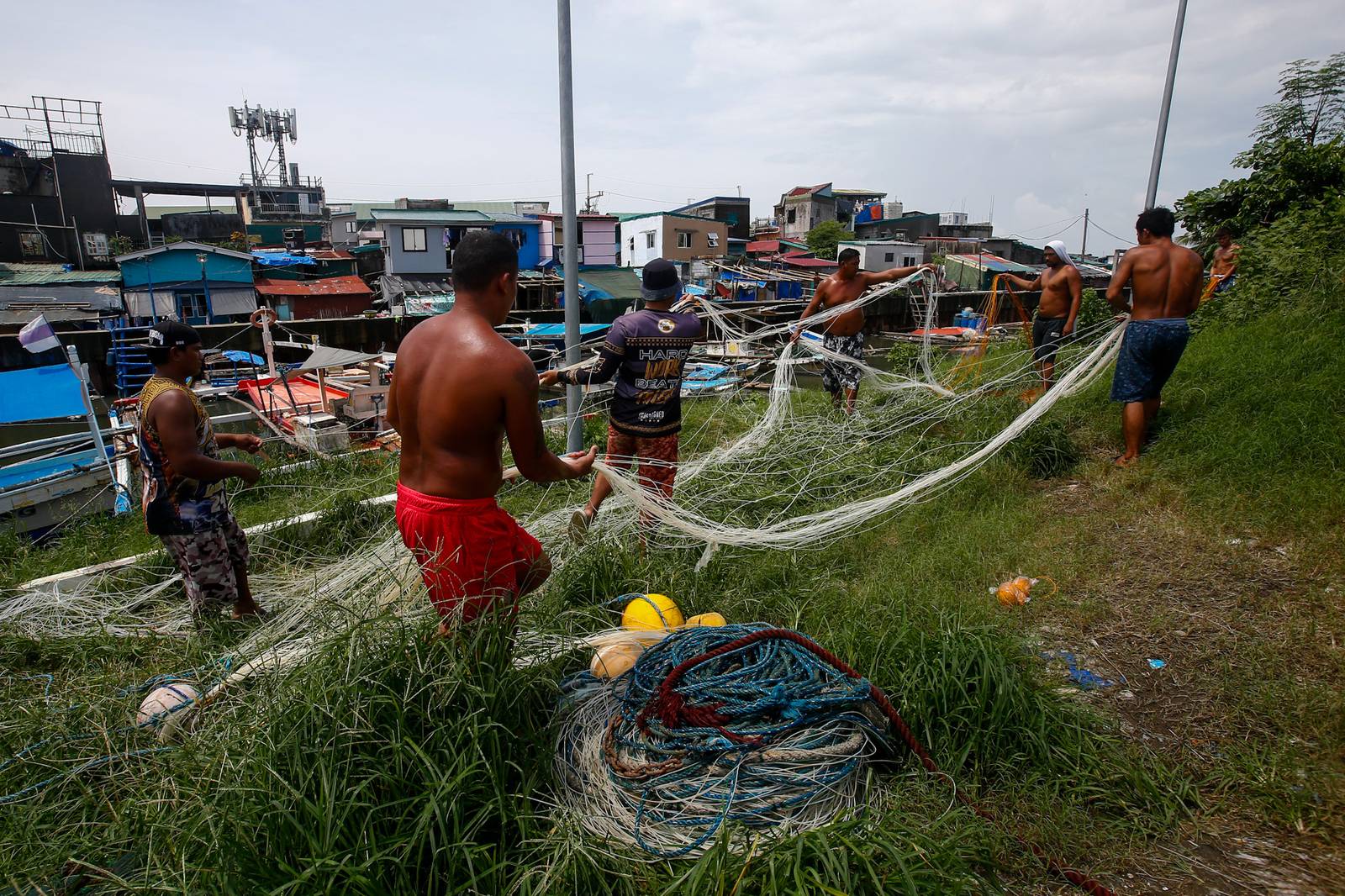 As the sun finally emerges, a group of fishermen make fishing nets at a vacant lot in Navotas City on 15 August 2026. Strong waves and heavy rains brought by the southwest monsoon, or habagat, have kept them from sailing for weeks.