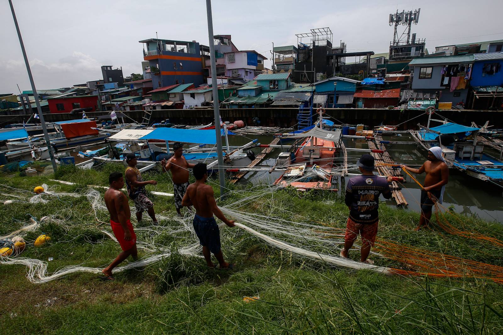 As the sun finally emerges, a group of fishermen make fishing nets at a vacant lot in Navotas City on 15 August 2026. Strong waves and heavy rains brought by the southwest monsoon, or habagat, have kept them from sailing for weeks.