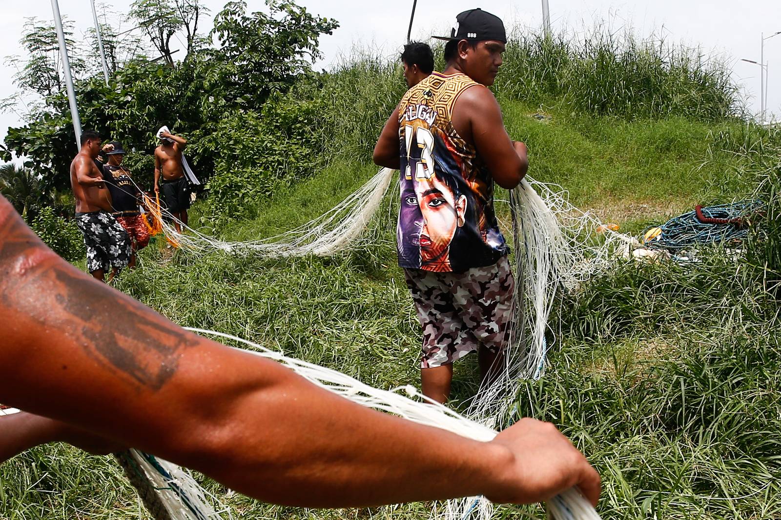 As the sun finally emerges, a group of fishermen make fishing nets at a vacant lot in Navotas City on 15 August 2026. Strong waves and heavy rains brought by the southwest monsoon, or habagat, have kept them from sailing for weeks.