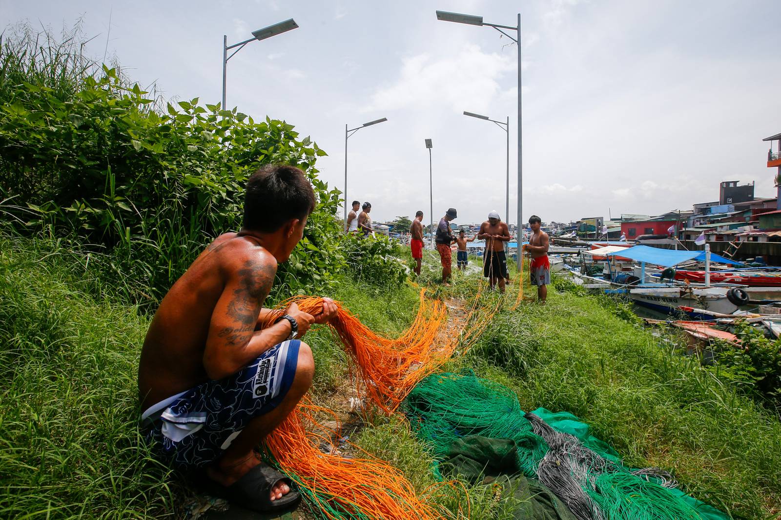 As the sun finally emerges, a group of fishermen make fishing nets at a vacant lot in Navotas City on 15 August 2026. Strong waves and heavy rains brought by the southwest monsoon, or habagat, have kept them from sailing for weeks.
