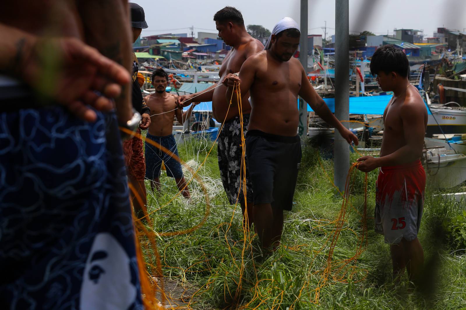As the sun finally emerges, a group of fishermen make fishing nets at a vacant lot in Navotas City on 15 August 2026. Strong waves and heavy rains brought by the southwest monsoon, or habagat, have kept them from sailing for weeks.