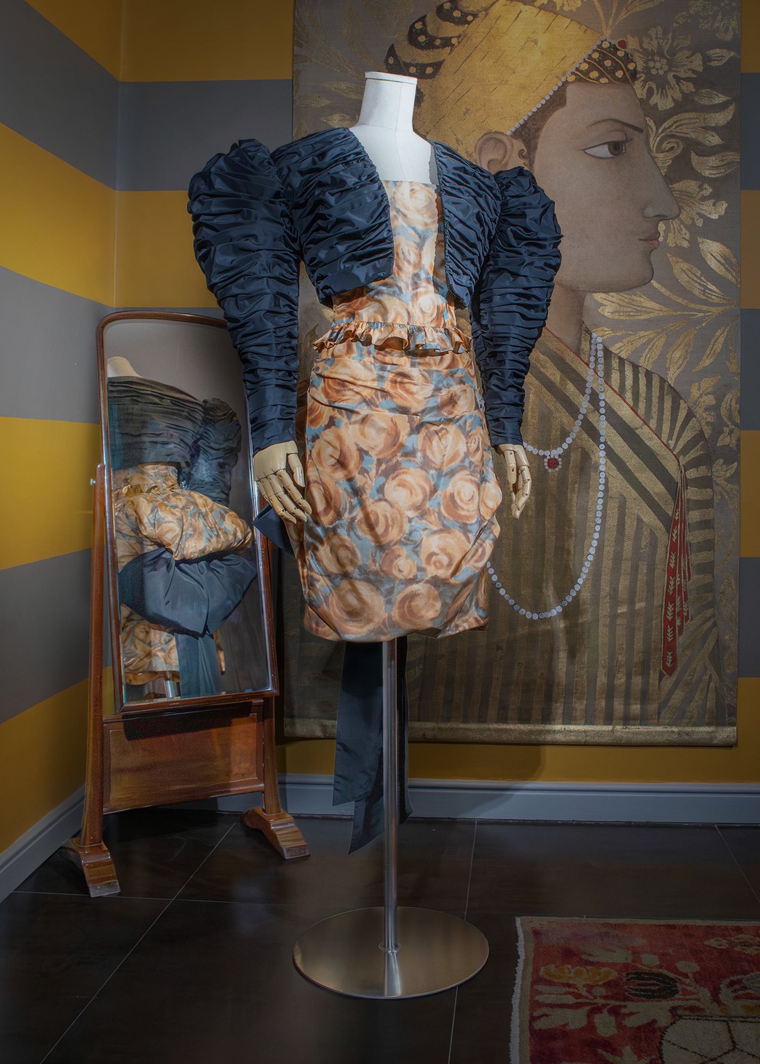 Two-piece ensemble floral dress in butterscotch and dusty blue print, featuring ruched detailing and a bustle skirt accented by a large bow, paired with a cropped ruched overtop with gigot sleeves.