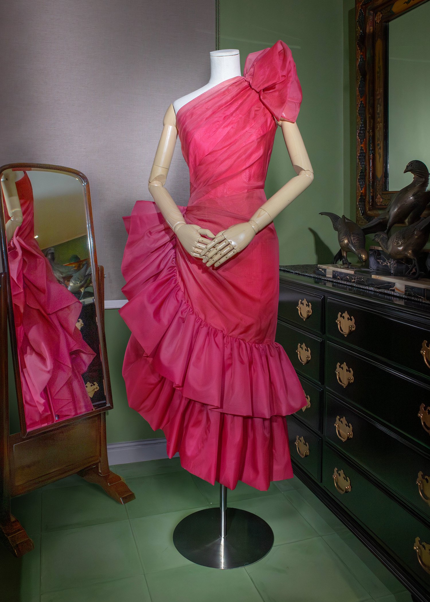 Salmon-pink pleated dress of silk organdy with a 3D floral appliqué on the shoulder and a layered ruffled hem.