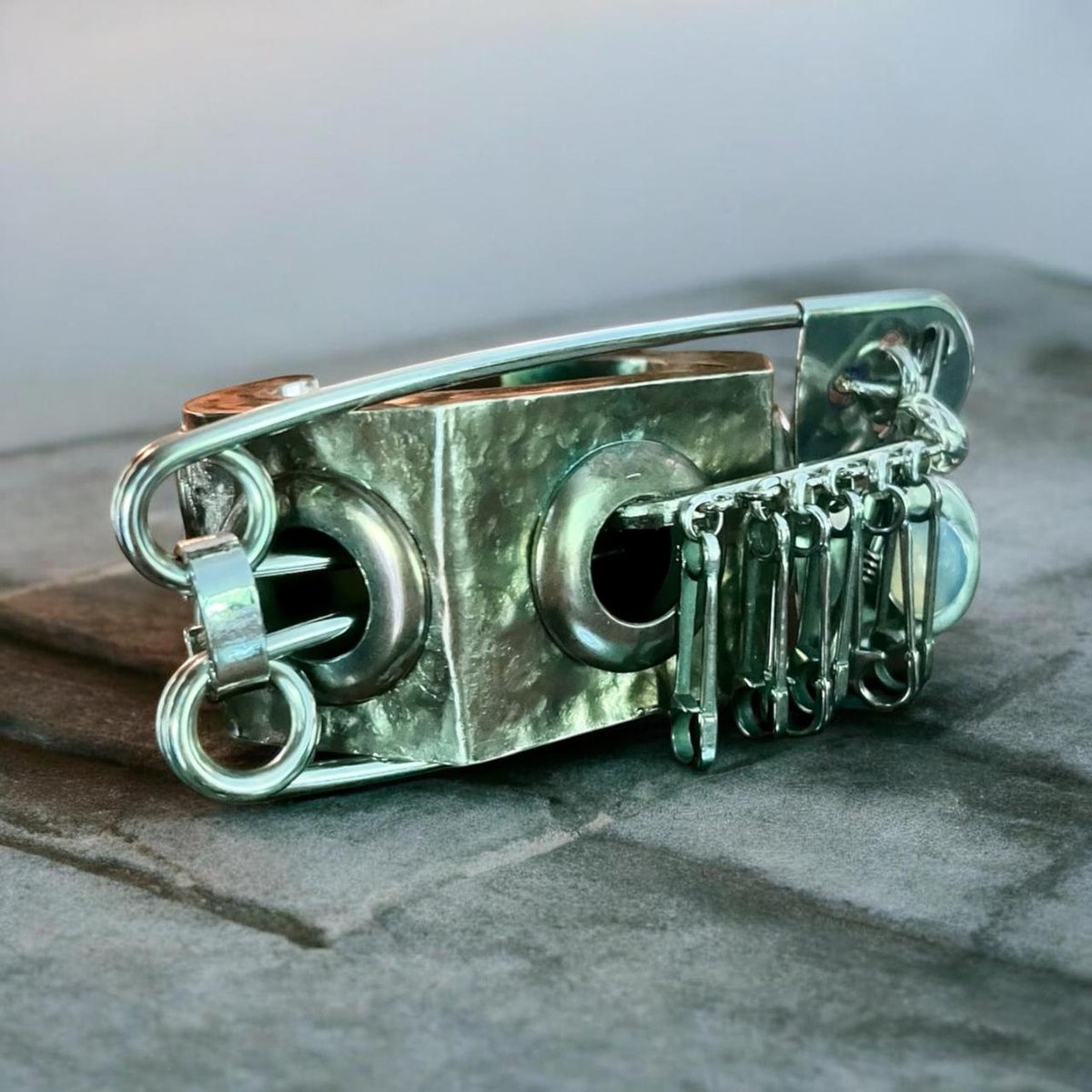oxidized and distressed sculptural cuff, accented by oversized safety pins which are lodged into the embedded gromets.