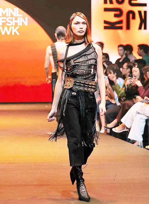 AVANT-GARDE black textured top, a utility-style grommet belt, and fringed black trousers.