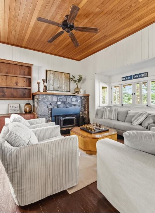 A stone fireplace anchors the living room with striped armchairs and a gray sofa beneath a wood-paneled ceiling fan.