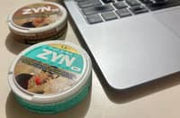 ZYN nicotine pouches sit beside a laptop.