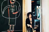 MUSICIAN and designer Lenny Kravitz stands barefoot in a hallway featuring black-and-white tile flooring alongside a large-scale painting by Jean-Michel Basquiat.