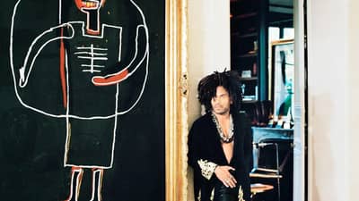 MUSICIAN and designer Lenny Kravitz stands barefoot in a hallway featuring black-and-white tile flooring alongside a large-scale painting by Jean-Michel Basquiat.