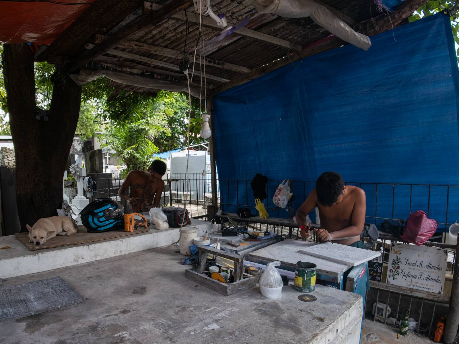 Eugene Gamurot and Cedrick Cayabyab carve a gravestone block at their makeshift workshop in Manila North Cemetery on 17 October 2026. Marble gravemarkers cost ₱500 to ₱5,000, depending on size, while granite markers start at ₱1,500.
