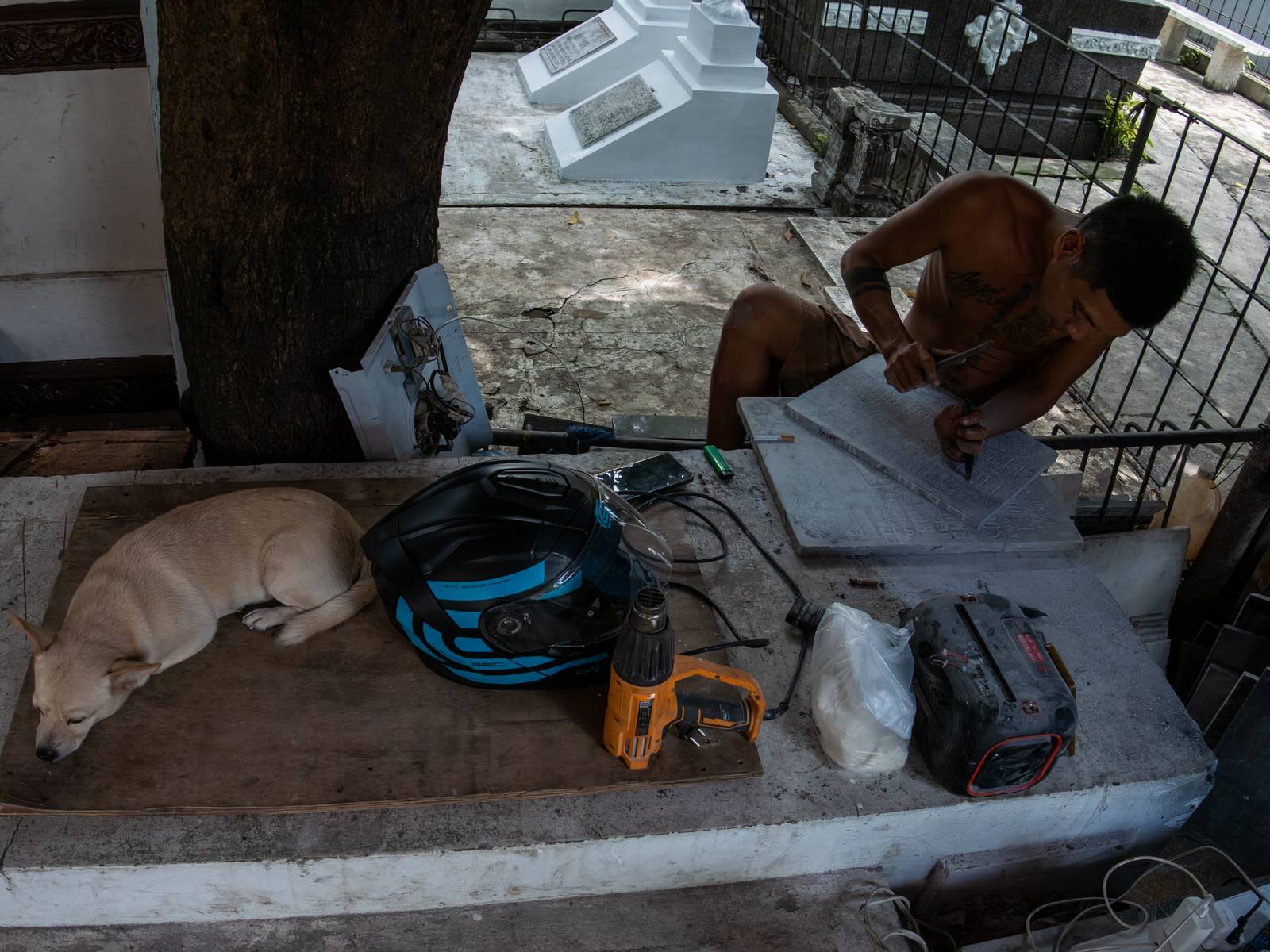 Eugene Gamurot and Cedrick Cayabyab carve a gravestone block at their makeshift workshop in Manila North Cemetery on 17 October 2026. Marble gravemarkers cost ₱500 to ₱5,000, depending on size, while granite markers start at ₱1,500.