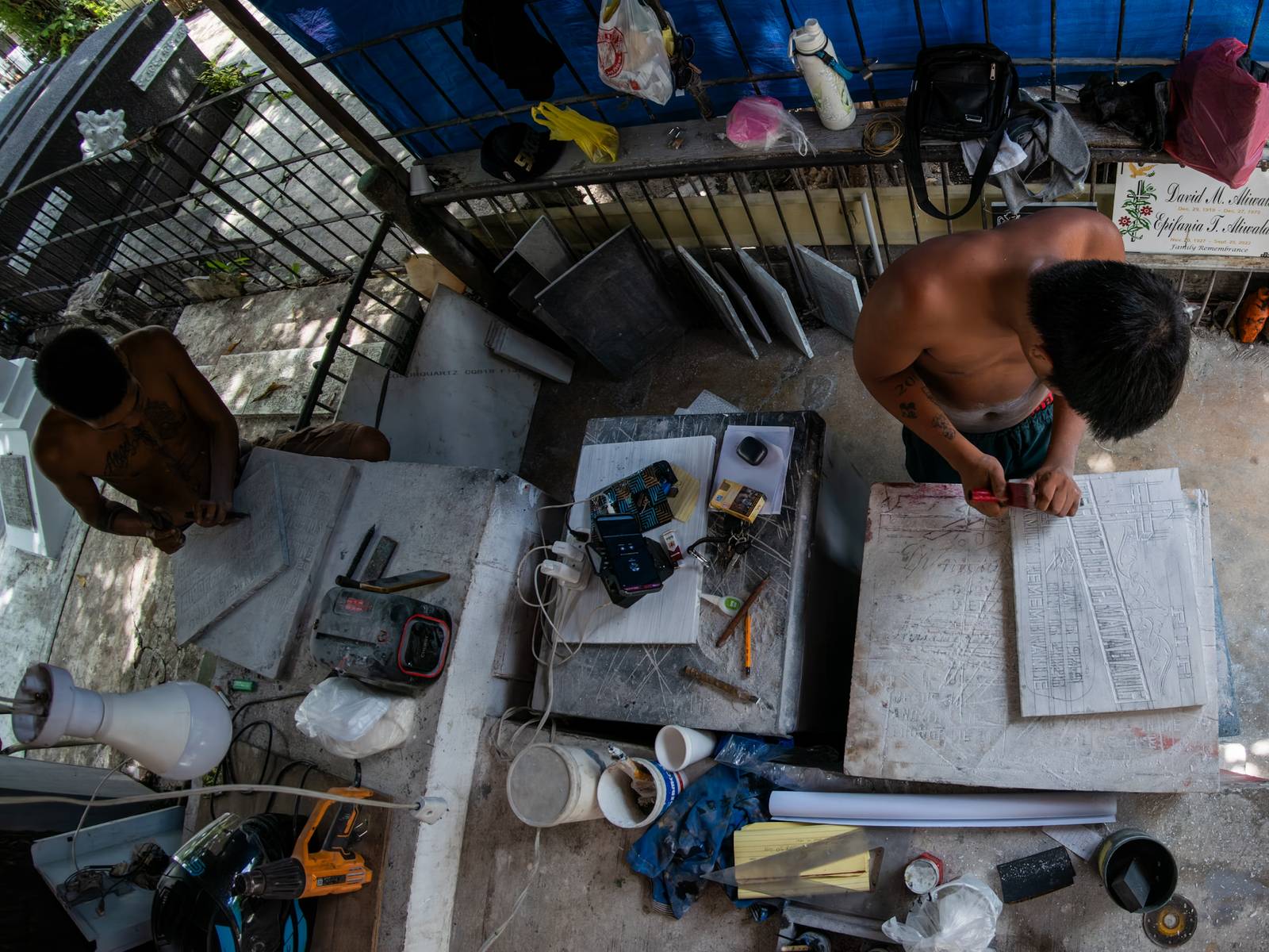 Eugene Gamurot and Cedrick Cayabyab carve a gravestone block at their makeshift workshop in Manila North Cemetery on 17 October 2026. Marble gravemarkers cost ₱500 to ₱5,000, depending on size, while granite markers start at ₱1,500.