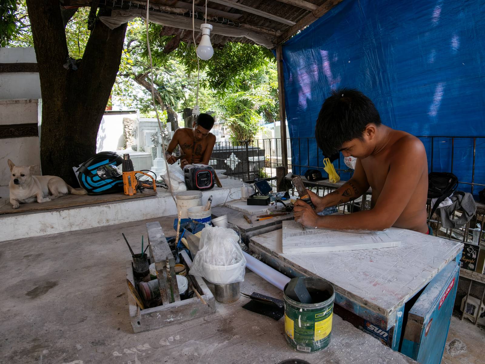 Eugene Gamurot and Cedrick Cayabyab carve a gravestone block at their makeshift workshop in Manila North Cemetery on 17 October 2026. Marble gravemarkers cost ₱500 to ₱5,000, depending on size, while granite markers start at ₱1,500.