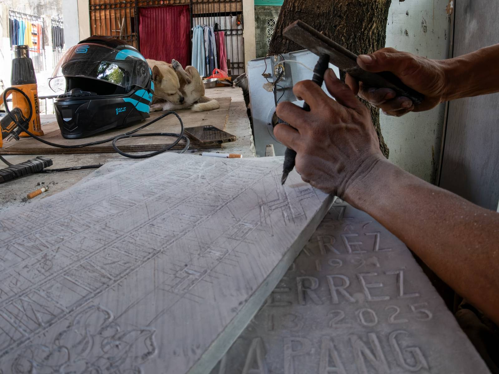 Eugene Gamurot and Cedrick Cayabyab carve a gravestone block at their makeshift workshop in Manila North Cemetery on 17 October 2026. Marble gravemarkers cost ₱500 to ₱5,000, depending on size, while granite markers start at ₱1,500.