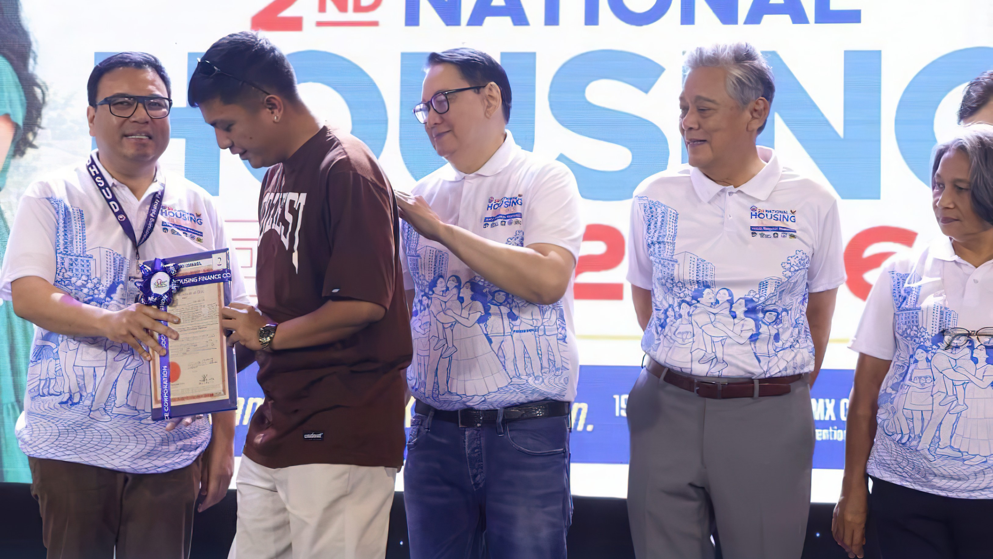 DEPARTMENT of Human Settlements and Urban Development Secretary Jose Ramon Aliling (left) hands over a land title to a beneficiary —  one of five members of the Kapisanan sa Landas ng Paninirahan Inc. — under the Social Housing Finance Corporation’s Community Mortgage Program — one of the SHFC’s flagship program under the Marcos administration’s Expanded Pambansang Pabahay para sa Pilipino Program during the 2nd National Housing Expo at  SMX Convention Center on 19 October 2026. With Secretary Aliling are (from left) SHFC president and CEO Federico Laxa, National Home Mortgage Finance Corporation president Renato Tobias, and Pag-IBIG Fund chief executive officer Marilene Acosta.