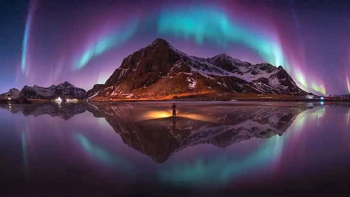 HIS winning photograph, The Emerald Arch Over Lofoten, Norway, captures the Northern Lights forming a sweeping arch above a mountain and reflecting across the water.